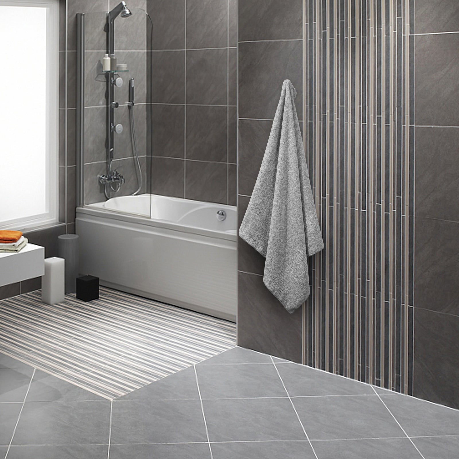 Modern bathroom with gray tiles, a bathtub, and a towel hanging on a rack.