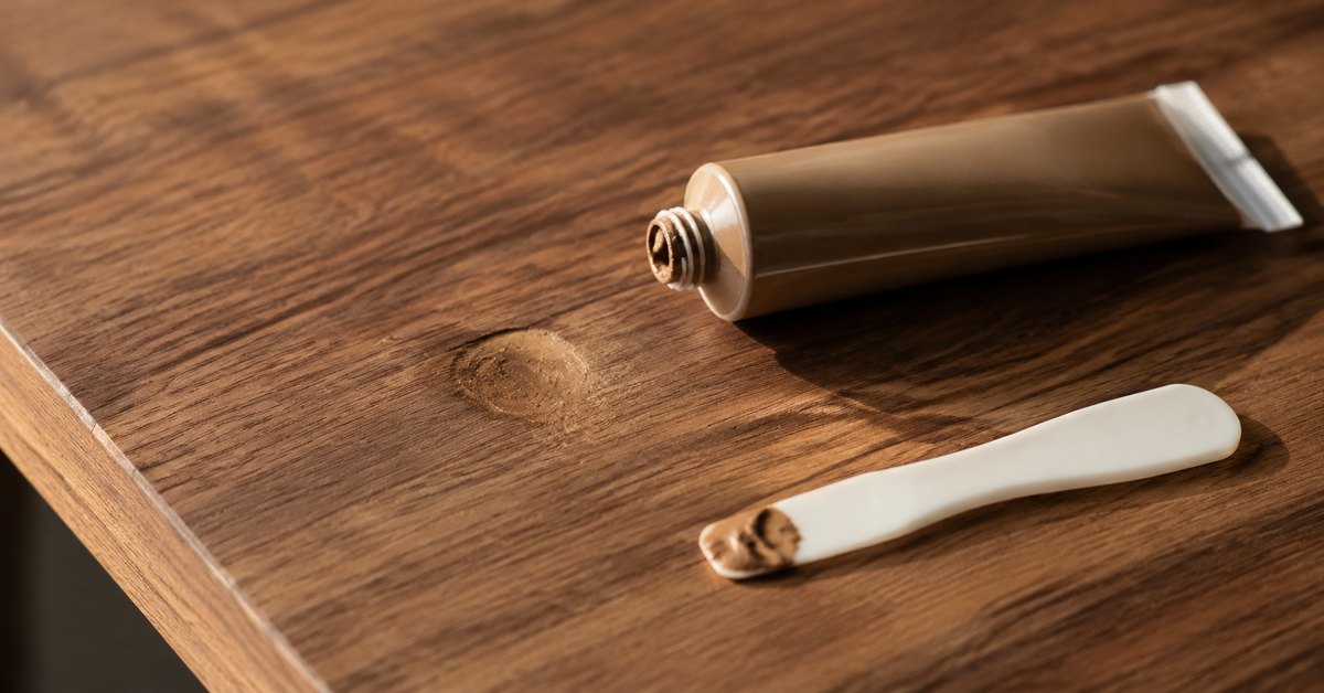 Shallow depression in a wooden furniture repair viewed under side lighting beside a small spreader